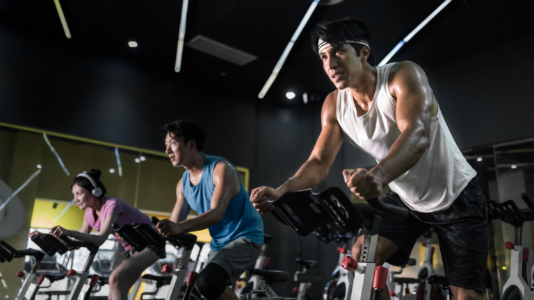 Study hints at the ‘optimal’ combo of sleep, diet and exercise to extend lifespan Young people riding stationary bike during indoor cycling class in gym.