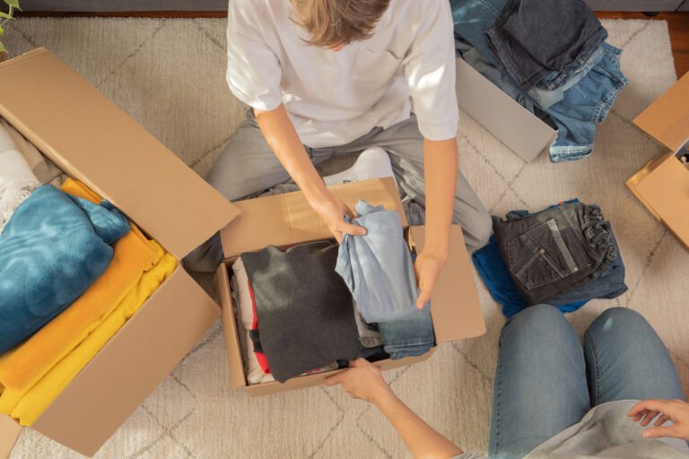 Woman and child sorting clothes and packing into cardboard box. (iStock-#1442828646 │ vejaa)