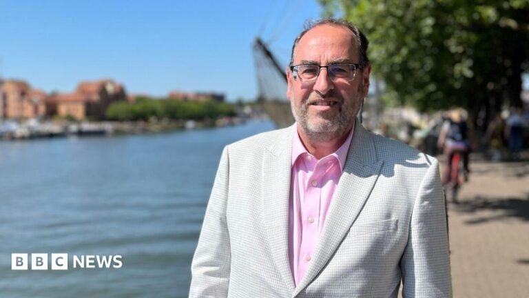 Bristol council leader opposes Green Party anti-Zionist motion A man in a grey suit jacket is pictured standing, looking at the camera. He's wearing a pink shirt, and behind him is a large harbourside and body of water.